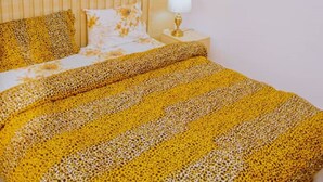 Una cama con una colcha de estampado de leopardo, una lámpara de noche y un almohadón con motivos florales.