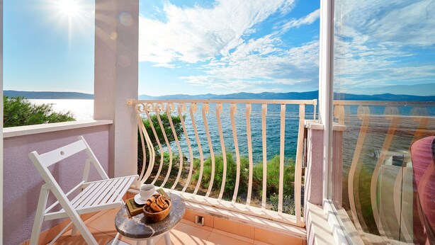 A balcony with a white chair, a small table with a bowl of cookies, and a view of the sea and mountains. - Sun Spalato Hills 8 (Split)