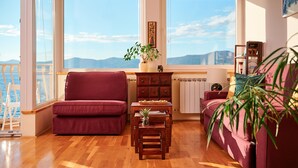 A living room with a wooden floor, a red sofa, a small wooden table with a plant, and a view of the sea through large windows. - Sun Spalato Hills 8 (Split)