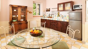 A kitchen with a round glass table, white chairs, a fruit bowl, wooden cabinets, and a stainless steel refrigerator. - Sun Spalato Hills 8 (Split)