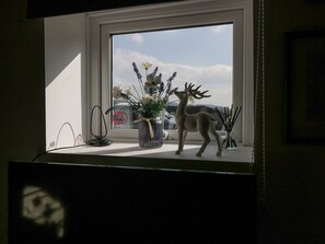 A window sill with a vase of flowers, a deer's figurine, and a no parking sign in the background. - High Wreah Bolt Hole (Whitehaven)