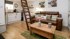 A cozy living room with a brown leather sofa, a wooden coffee table, and a ladder leading to a loft bedroom. - High Wreah Bolt Hole (Whitehaven)