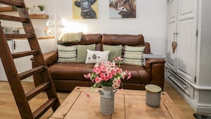 A living room with a brown leather sofa, a wooden coffee table with a vase of pink flowers, and a ladder against the wall. - High Wreah Bolt Hole (Whitehaven)
