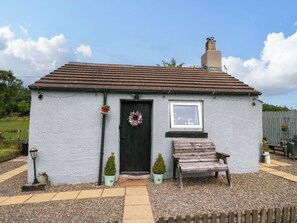 A small, single-story cottage with a black door, a small window, and a wooden bench outside. - High Wreah Bolt Hole (Whitehaven)