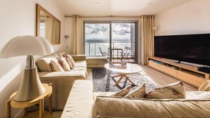 Une chambre d’hôtel moderne dotée d’une grande télévision à écran plat, d’un canapé, d’une table basse et d’un balcon offrant une vue sur la mer.