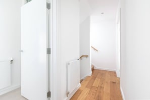 A hallway with white walls, a radiator, and a wooden floor.