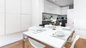 Une cuisine moderne avec des meubles blancs, une table à manger pour quatre personnes et un petit îlot central équipé d’appareils de cuisine.