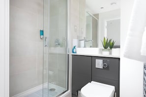A modern bathroom with a glass shower enclosure, a white sink, and a dark-toned cabinet.