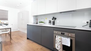 Une cuisine moderne avec des meubles blancs, un four en acier inoxydable et une table à manger en bois.