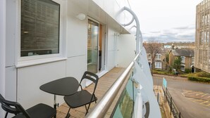 Een balkon met een tafel en stoelen, een glazen hekwerk en uitzicht op woongebouwen.