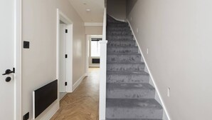 A staircase with a handrail, a door with a black handle, and a light switch on the wall.