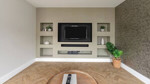 A modern living room with a flat-screen TV mounted on a wall, wooden flooring, and a potted plant.