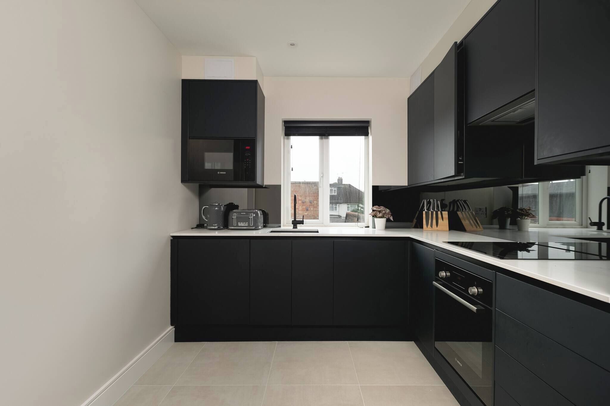 A modern kitchen with black cabinets, a built-in oven, a microwave, and a window with a view of buildings.