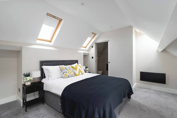 A bedroom with a bed, a nightstand, a lamp, a window, and a built-in heater.