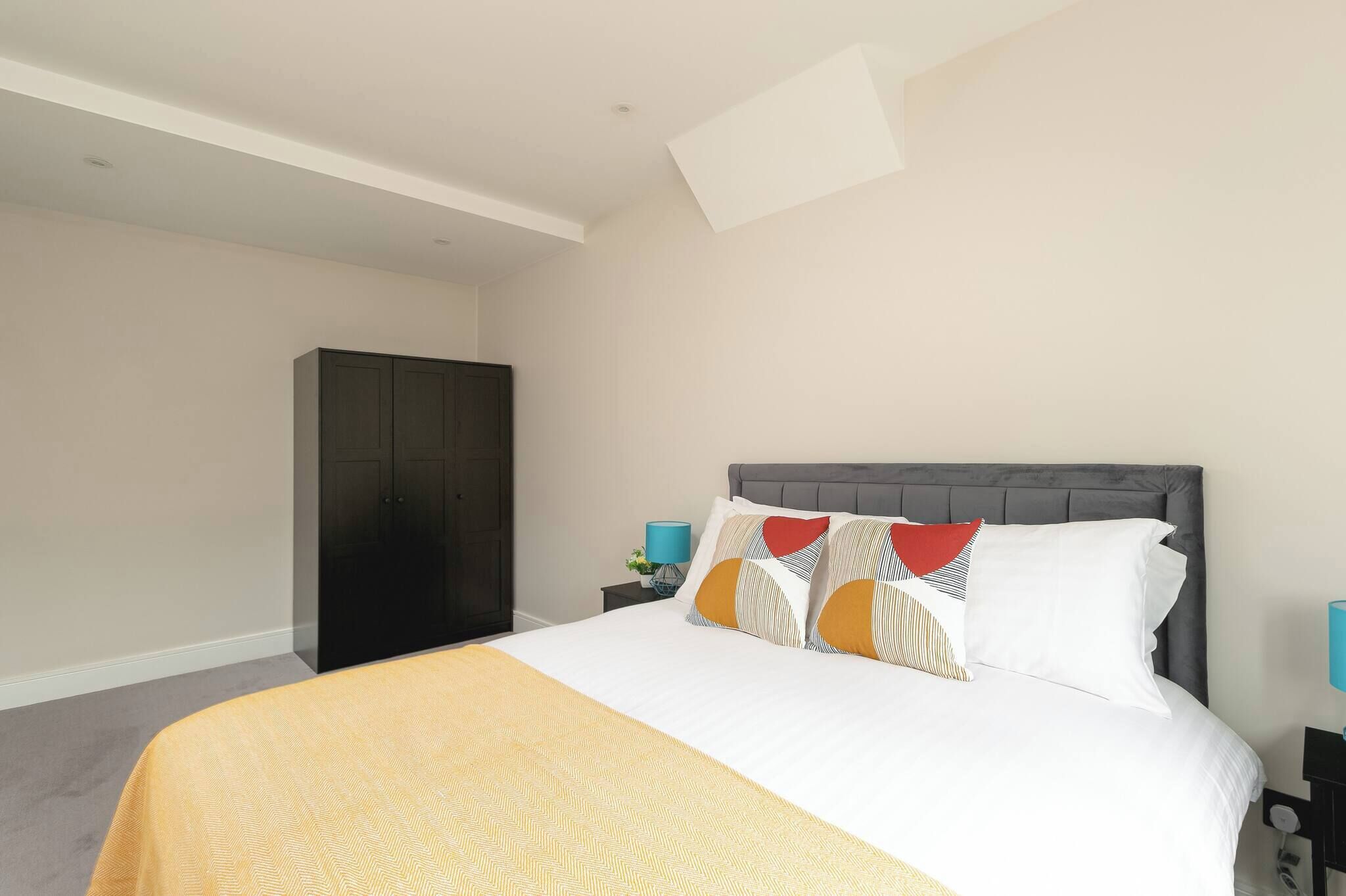 Une chambre à coucher comprenant un lit, une armoire, une table de chevet avec une lampe et une étagère fixée au mur.