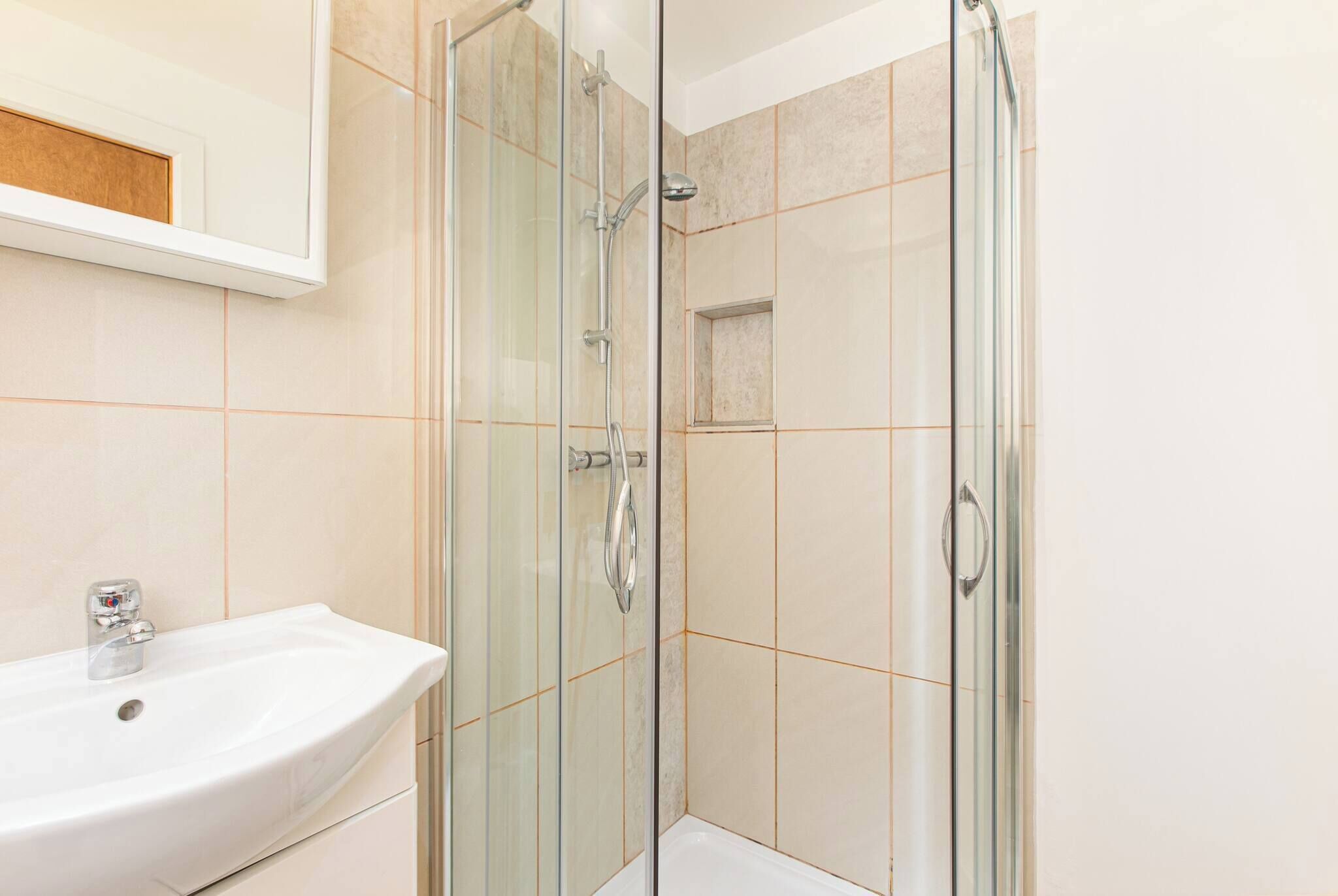 A bathroom with a glass-enclosed shower, a sink, and a mirror.