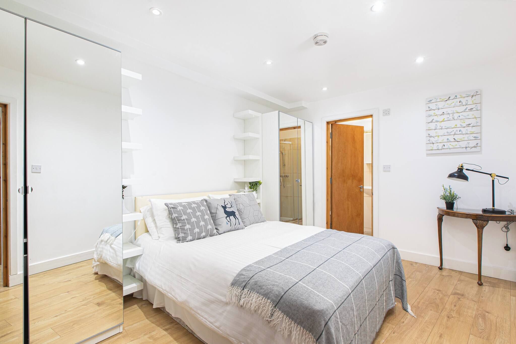 A modern bedroom with a bed, bedside table, and a mirror.