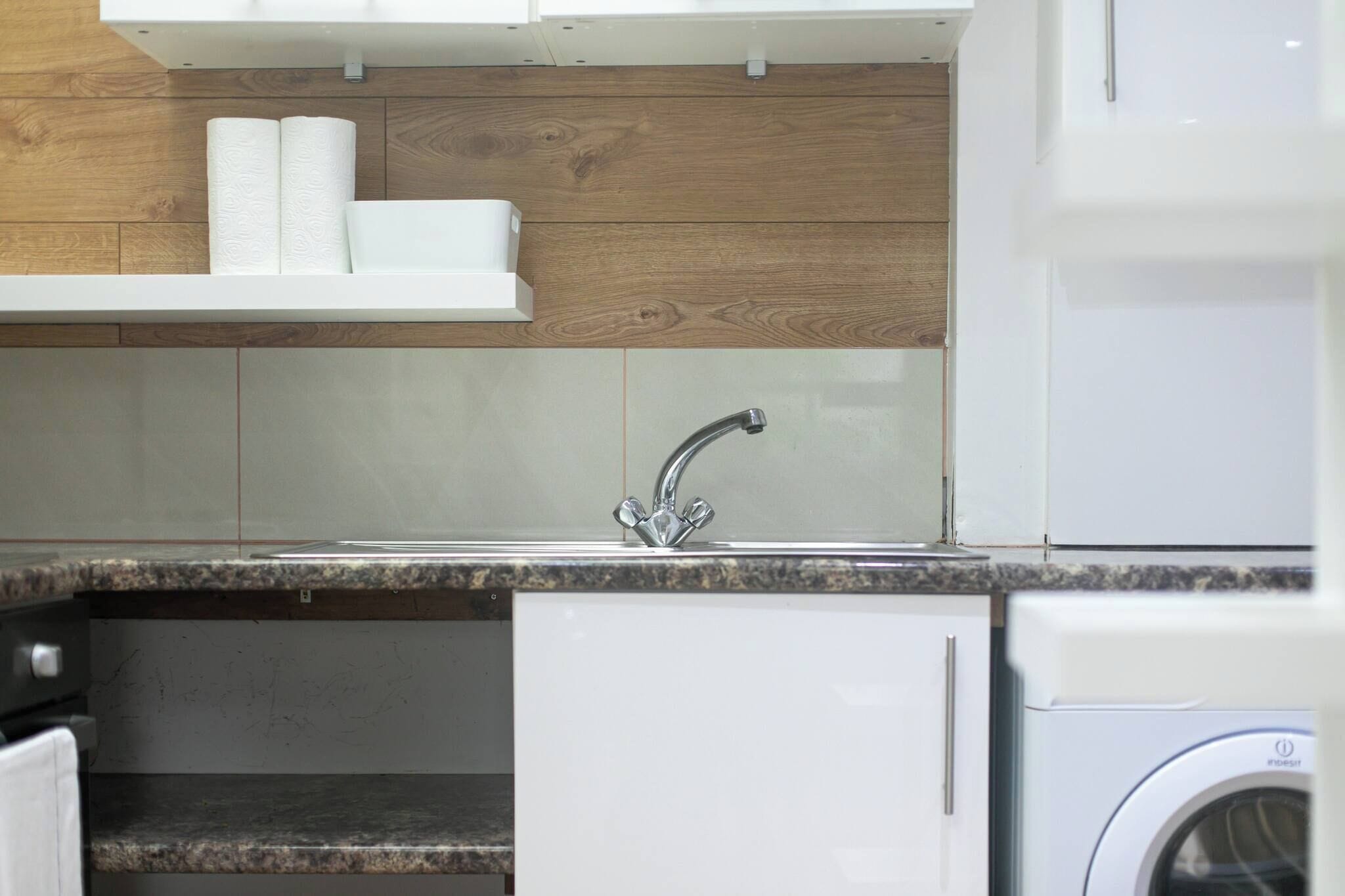A kitchen with a sink, wooden wall paneling, and a washing machine.