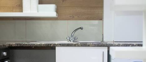 A kitchen with a sink, wooden wall paneling, and a washing machine.