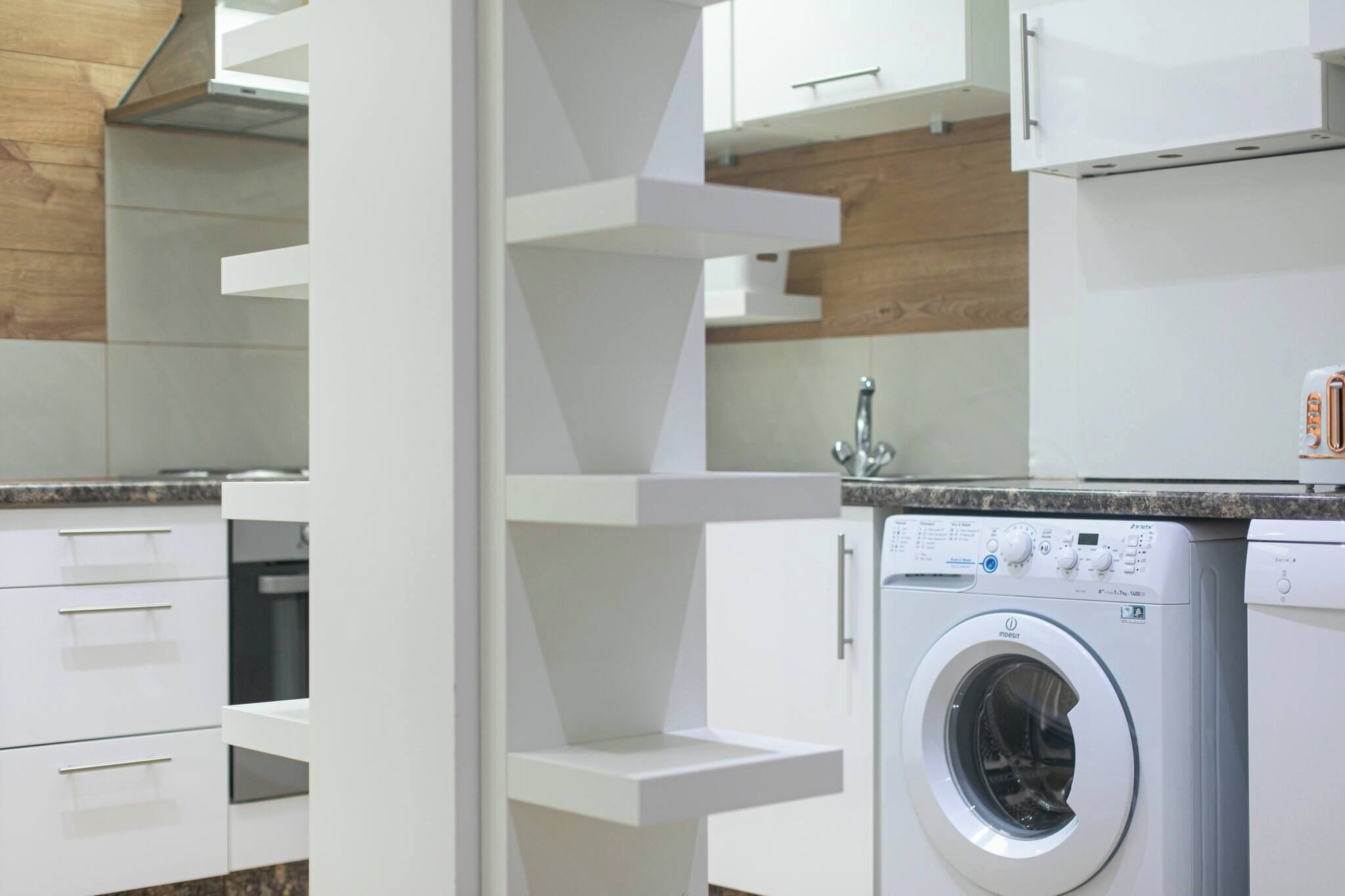 A modern kitchen with white cabinetry, a built-in washing machine, and a granite countertop.