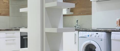 A modern kitchen with white cabinetry, a built-in washing machine, and a granite countertop.