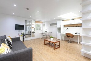 Un salon moderne avec un canapé gris, une table basse, un téléviseur et un coin repas comprenant une table et des chaises en verre.