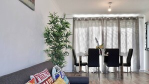 Un salon avec un canapé, une table à manger avec des chaises, une plante en pot et une fenêtre avec des rideaux.