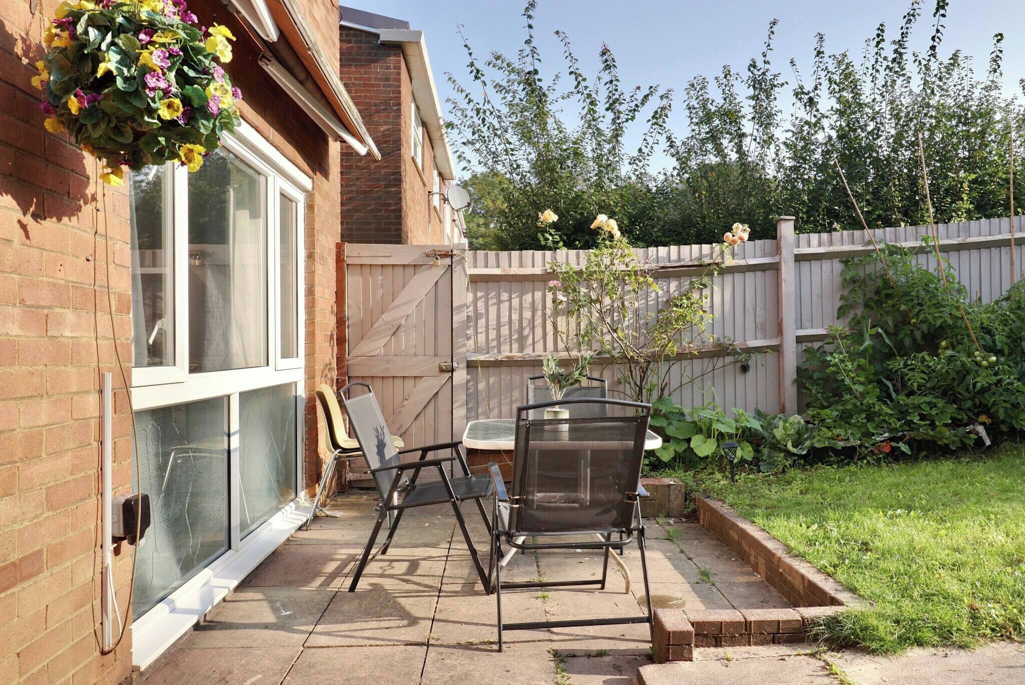 A patio with a table and chairs, a hanging flower basket, and a brick wall.