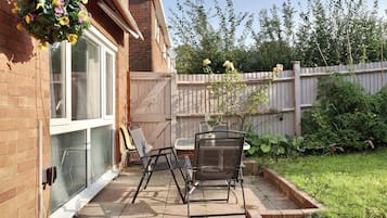 A patio with a table and chairs, a hanging flower basket, and a brick wall.