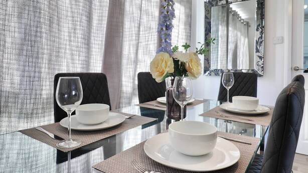 Un coin repas avec une table en verre, des chaises noires, des assiettes blanches et un vase rempli de fleurs.