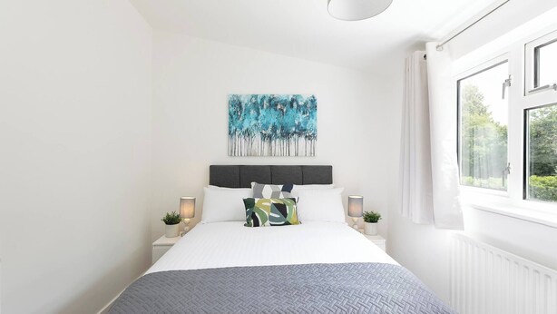 A bedroom with a bed, a painting, bedside lamps, and a window. - Skyvillion - Lush 2 Bed Hydean Way House & Garden (Stevenage)