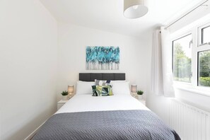 A bedroom with a bed, a painting, bedside lamps, and a window. - Skyvillion - Lush 2 Bed Hydean Way House & Garden (Stevenage)
