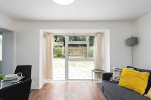 Ett rum med ett matbord, stolar, en soffa med kuddar, en lampa och en skjutdörr i glas som leder ut till ett utomhusområde.