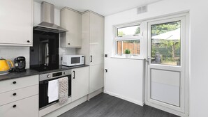 A kitchen with white cabinets, a microwave, a kettle, and a stove. - Skyvillion - Lush 2 Bed Hydean Way House & Garden (Stevenage)