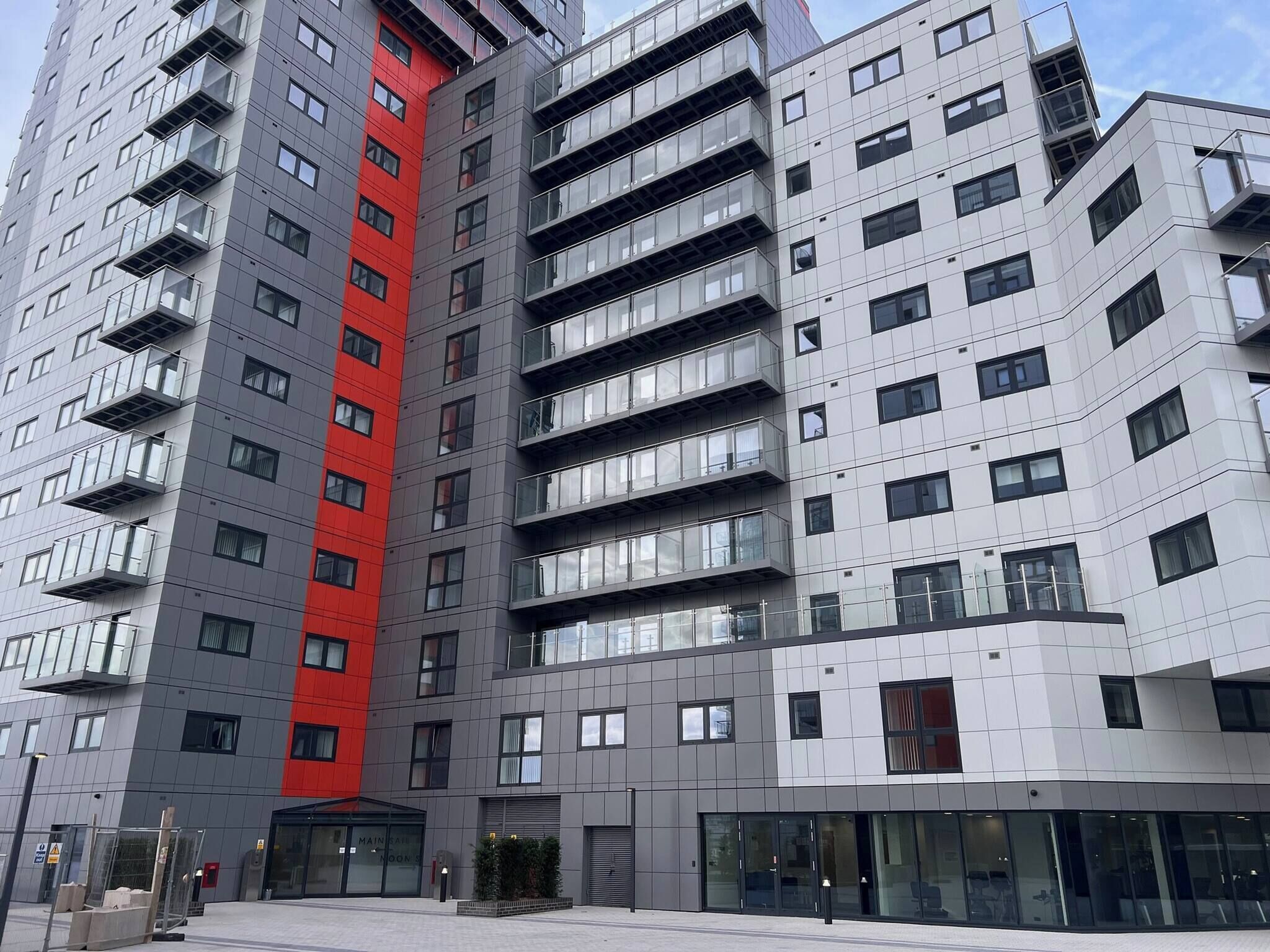 A multi-story building with balconies, a red accent wall, and a glass entrance.