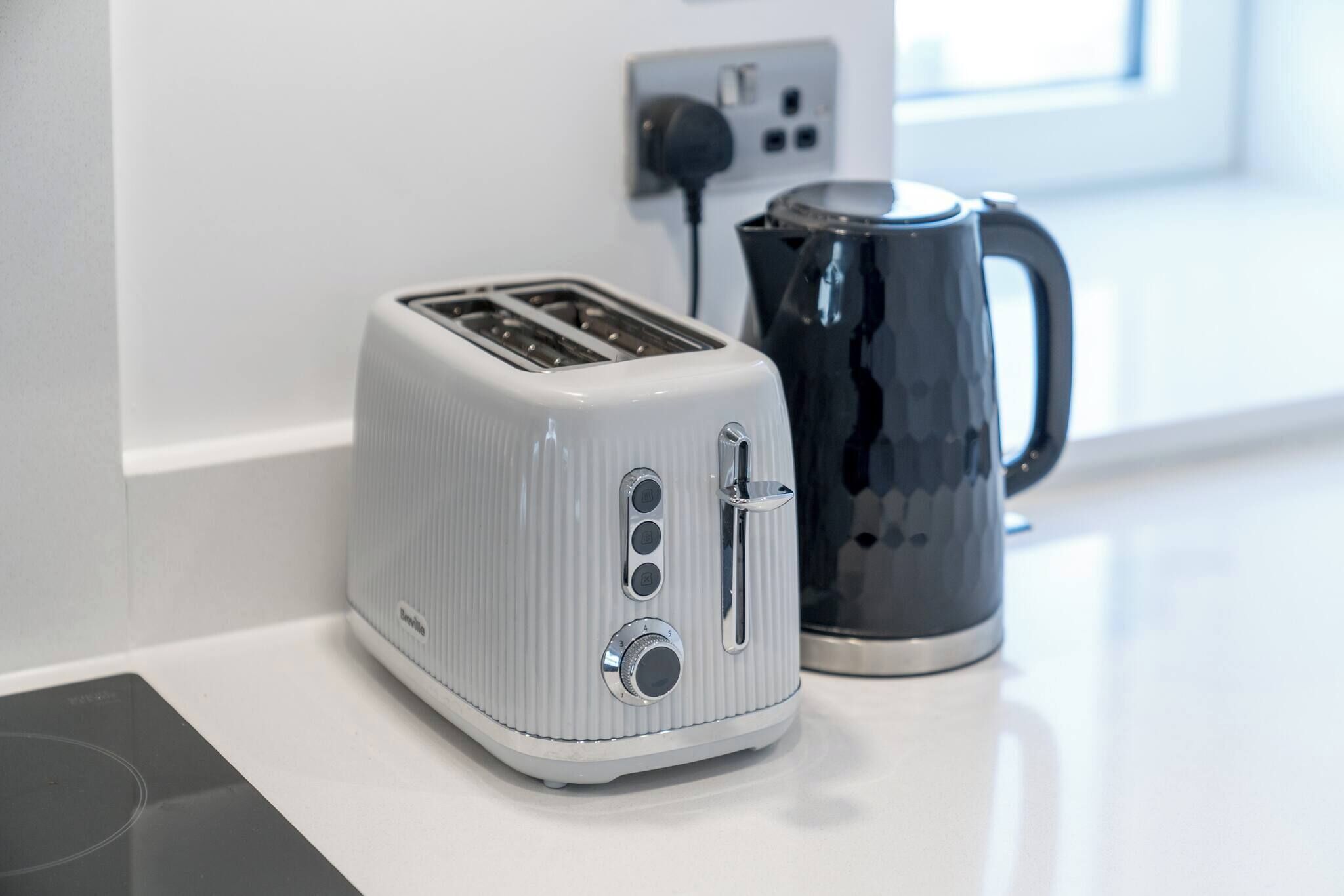 A kitchen with a white toaster, a black coffee pot, and a power outlet.