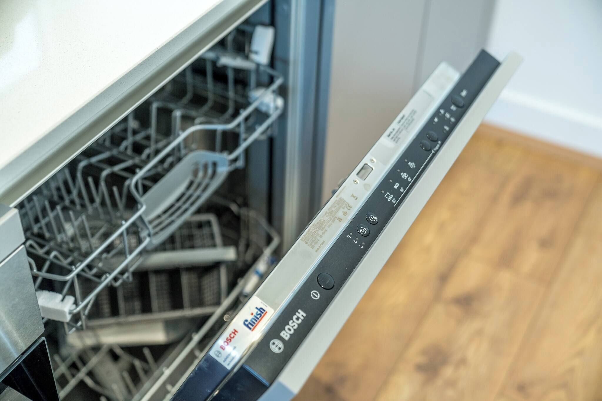 Un lavavajillas Bosch con panel de control, puerta abierta y un estante lleno de platos.