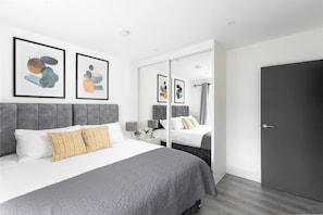 A modern hotel room with a large bed, a mirror, and abstract art on the wall.