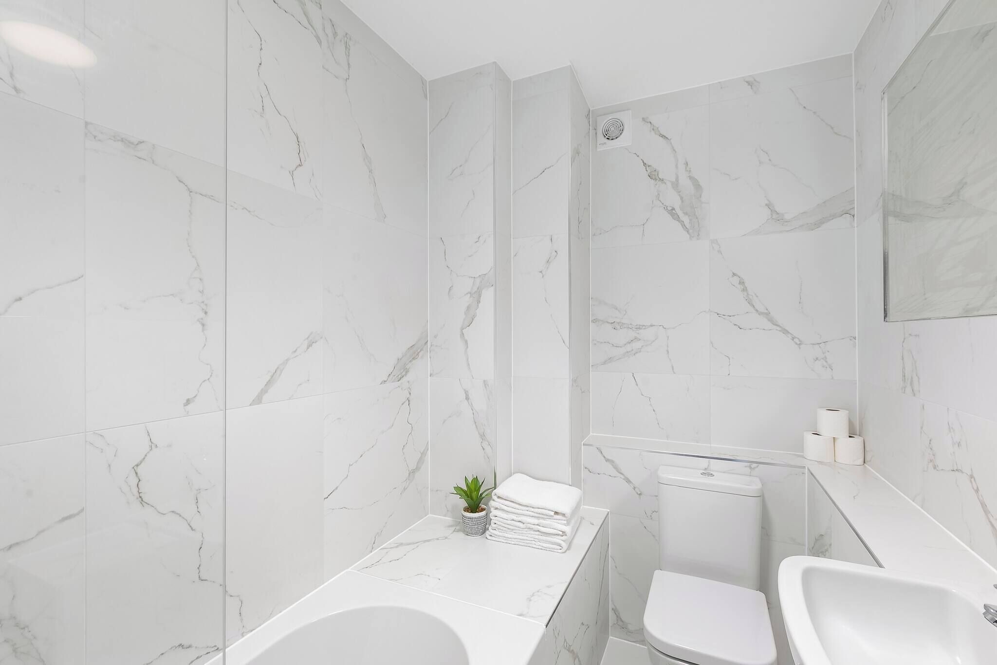 A modern bathroom with white marble tiles, a bathtub, a toilet, and a sink.