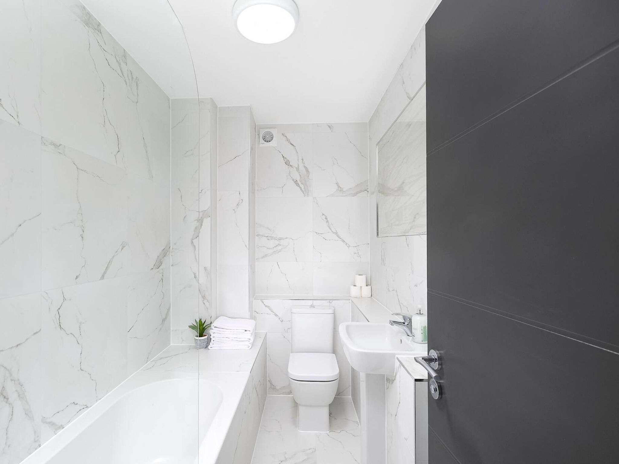 A modern bathroom with a bathtub, toilet, and sink, all with marble walls.