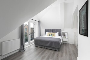 A modern bedroom with a sloped ceiling, a large bed, a nightstand, and a view through a glass door.