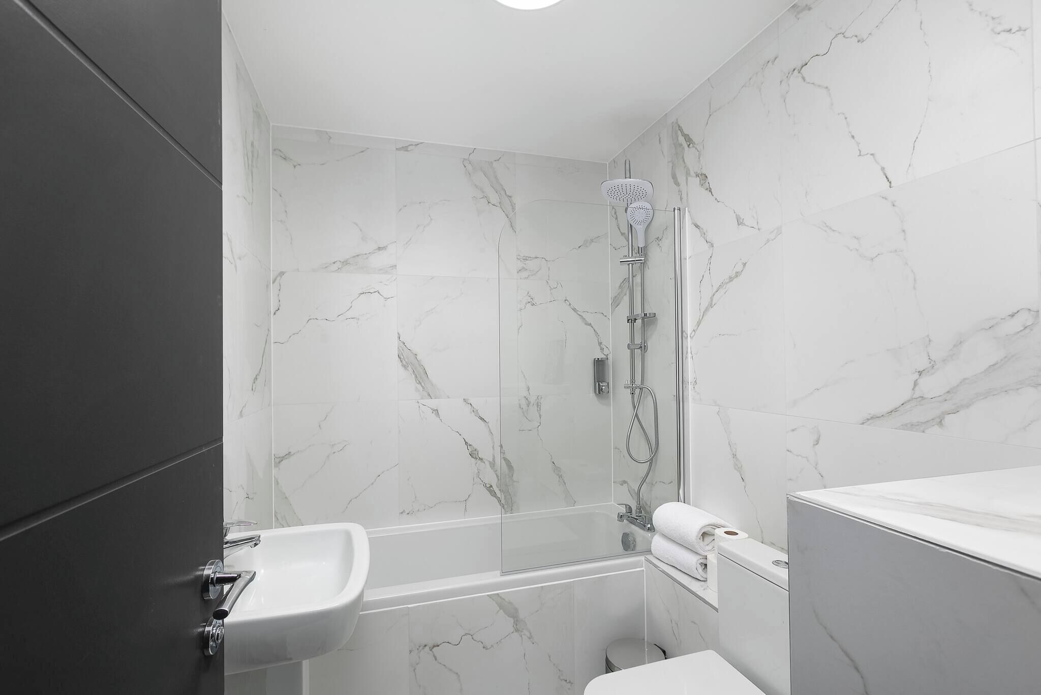 A modern bathroom with a glass-enclosed shower, a white sink, and a marble-tiled wall.