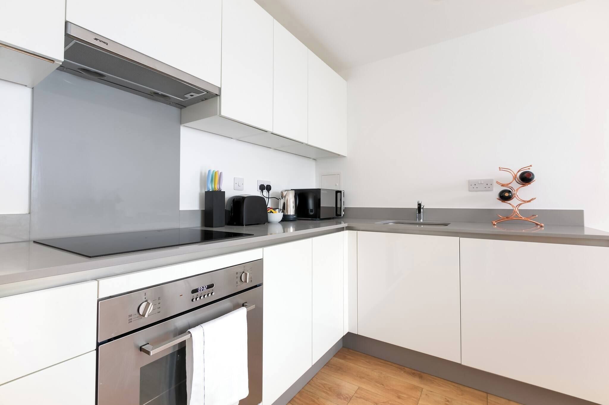 A modern kitchen with white cabinets, a stainless steel range hood, a built-in oven, and a black coffee maker.