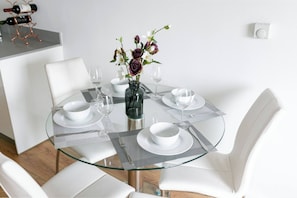 Un comedor moderno con una mesa de vidrio, sillas blancas y un jarrón con flores.