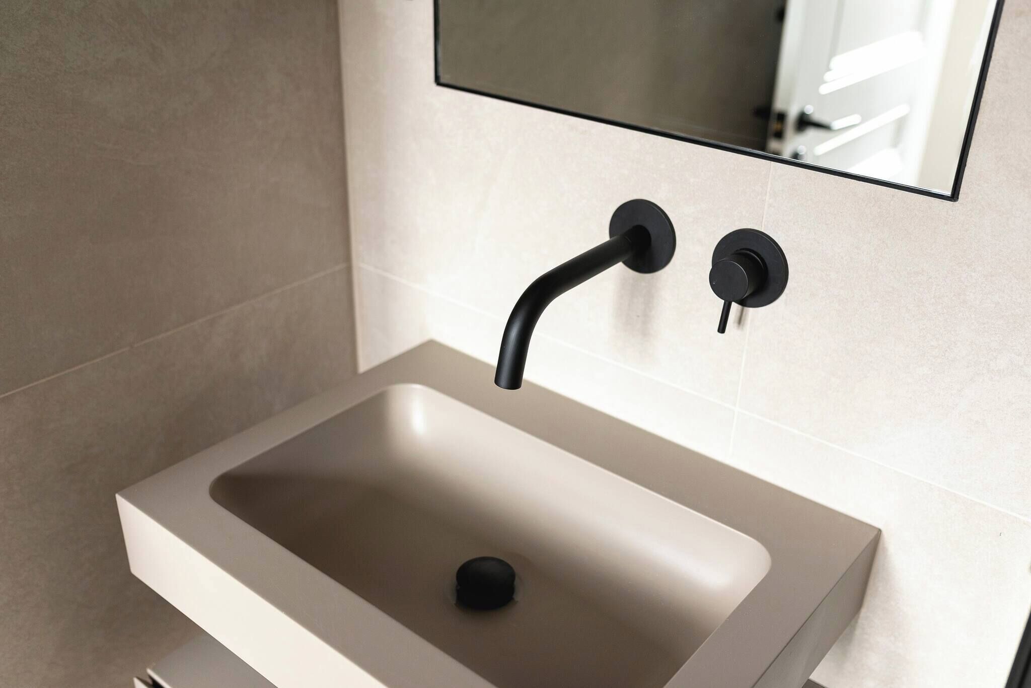 A modern bathroom with a rectangular sink, a mirror above it, and a wall-mounted faucet.