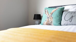 A bed with a yellow blanket, a black lamp, and two pillows with a rabbit design and a partial text design. - Skyvillion -1bed Cockfosters Near Alexandra Palace (Barnet)