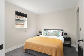 Un dormitorio con cama, mesita de noche, ventana con persianas y puerta.