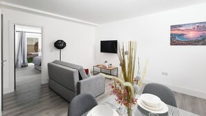Uma sala de estar moderna com sofá, mesa de jantar e televisão de tela plana na parede.