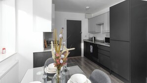 Cozinha moderna com armários escuros, mesa de jantar com um vaso de flores e vista para o cômodo adjacente.