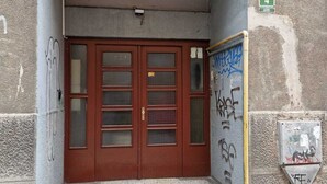 Une entrée d’immeuble avec une porte rouge à deux battants, un petit auvent et un panneau indiquant la sortie de secours, fixé au mur.